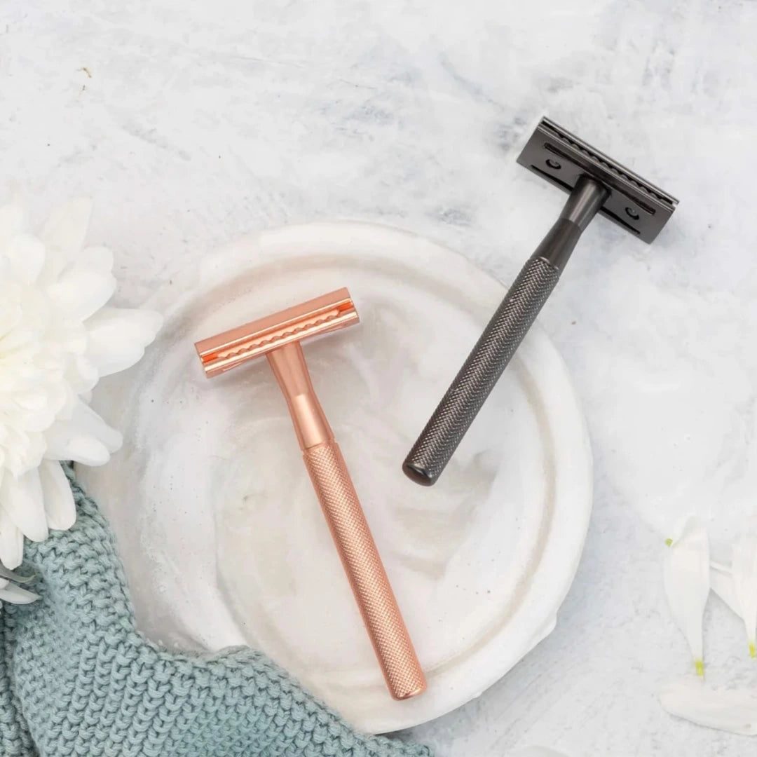 Two safety razors, one rose gold and one black, on a white dish with a light background.
